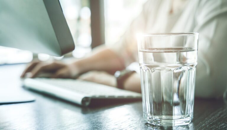 glass of alkaline water next to a computer