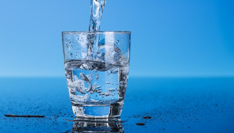 Purified water being poured into a glass with two glasses of purified water kept beside it.