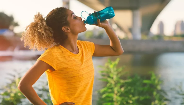 A female runner taking a break to drink from her water bottle.