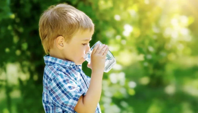 A little boy drinking water out of a glass.