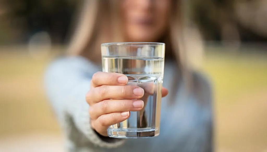 A blurred image of a woman holding a glass of clean water. The glass is in focus.