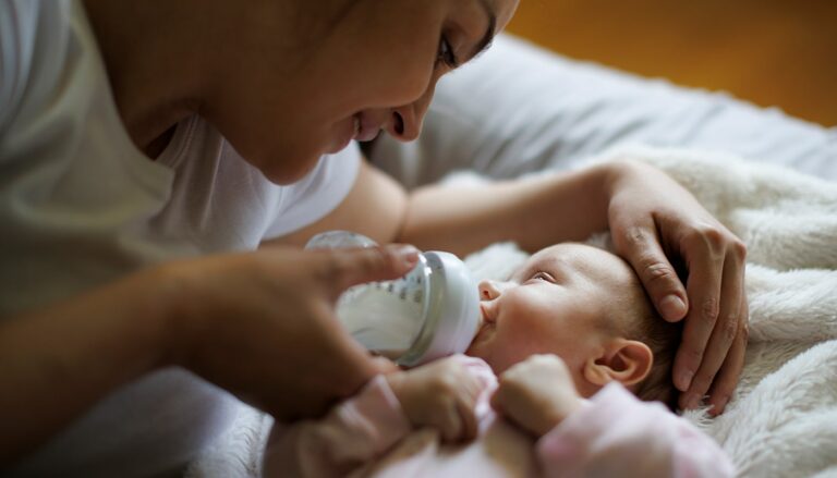 distilled water for baby formula feature - mother giving her newborn a bottle of formula